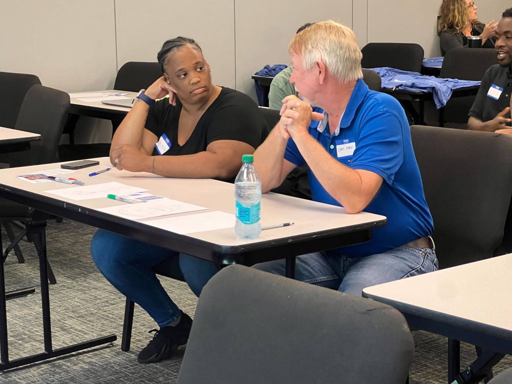 Two people seated at a table during a weatherization customer service class, listening attentively to each other.