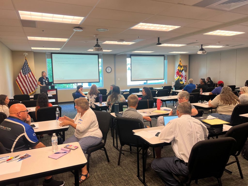 A classroom filled with students seated at tables, facing an instructor at the front who is speaking on weatherization customer service.
